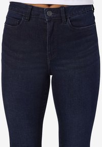 Mørk denim høytlivsjeans med knappelukking, frontlommer og en glatt tekstur med svakt falmet detaljer.