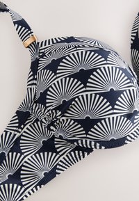 Soutien-gorge bleu marine avec motif coquille Saint-Jacques blanc, bonnets moulés, bretelle réglable et détail de quincaillerie dorée sur la bretelle.