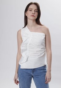 Hvid, top med én skulder, med voluminøse detaljer og plisseringer foran; lavet af glat stof. Båret med blåstribede denimjeans.