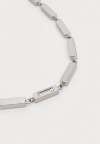 Collana in argento con maglie rettangolari, alternate a un accentuato gemma rettangolare trasparente, incisa con il nome del marchio.
