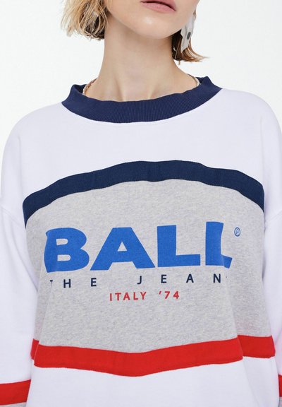 Le pull blanc présente un col côtelé bleu marine, un corps gris avec des rayures horizontales rouges et bleu marine, et une inscription audacieuse en bleu "BALL THE JEAN ITALY '74".