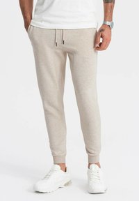 Beige sweatpants met zijzakken, elastische tailleband en enkels die zijn afgewerkt. Gemaakt van zachte stof met een subtiele textuur.