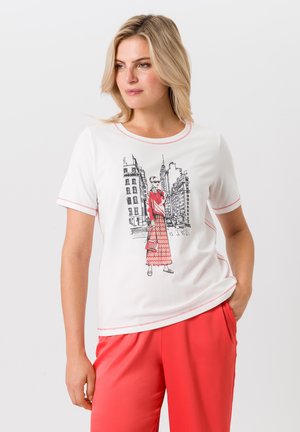 T-shirt blanc avec des accents rouges, présentant une illustration en noir et blanc d'une femme en tenue rouge contre un paysage urbain. Tissu doux.