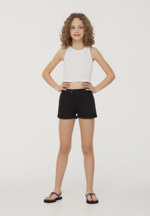 Shorts neri in cotone con vita regolabile, abbinati a un top corto bianco. Il modello si trova in piedi con le mani sui fianchi, indossando sandali neri.