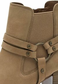 Bottine fauve avec corps en cuir texturé, panneau en maille, sangles réglables, accent métallique circulaire et talon empilé.