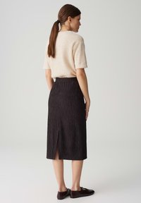 Maglione corto a maniche corte beige chiaro abbinato a una gonna midi nera a vita alta e texture, con uno spacco sul retro, completato da scarpe scure.