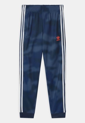 Marineblauwe Adidas trainingsbroek met witte zijstrepen, elastische tailleband, geribbelde enkels en rood Adidas-logo op de linker dij.