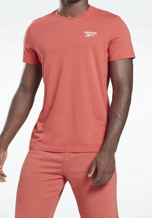 Homme portant un t-shirt à manches courtes et un short assortis rouge atténué Reebok sur un fond blanc uni.