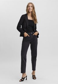 Svart kavaj över en figurnära svart topp, ihop med mörkgrå högmidjade jeans och svarta klacksandaler. Minimalistisk design och skräddarsydd passform.