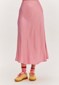 Ružová, splývavá midi sukňa vyrobená z hladkej tkaniny. Skombinovaná so žltými teniskami a ružovými ponožkami s červenými akcentmi. Jednoduchý dizajn, bez viditeľných vzorov.