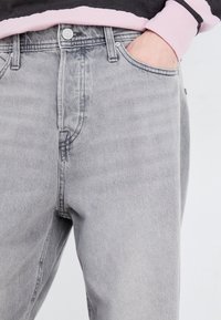 Jeans in denim grigio con una vestibilità rilassata, dotati di design a cinque tasche, chiusura con bottone e dettagli di leggera scoloritura sul tessuto.