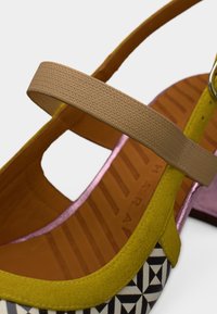 Πράσινο και μαύρο παπούτσι με σχέδιο, μπεζ λουράκι στον αστράγαλο, εσωτερικό από δέρμα και μοβ λεπτομέρεια στο πίσω μέρος. Ορατή υφή στη σόλα.