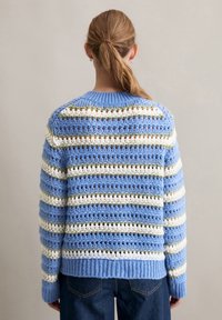 Niebiesko-biały sweter dzianinowy w paski z luźnym, otwartym wzorem. Posiada ściągacz przy kołnierzu i hemie, z zielonymi akcentami w postaci pasków.