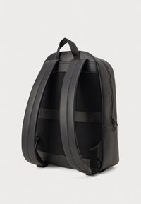 Čierny kožený ruksak s zakriveným tvarom, sieťovanou zadnou časťou, nastaviteľnými popruhmi a bočnou kapsou. Obsahuje hornú rukoväť a zipsové zapínanie.