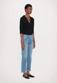 Top de punto negro con cuello y mangas tres cuartos, combinado con jeans de pierna recta azul claro y bailarinas negras.