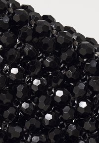Schwarze facettierte Perlen mit glänzender Textur, dicht zusammengefügt, die eine hexagonale Form und reflektierende Oberflächen zeigen.
