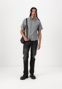 Cămașă cu mâneci scurte în dungi alb-negru, combinată cu blugi negri de denim. Modelul poartă o geantă mică de umăr neagră și cizme groase negre.