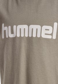 Grå bomulls-t-shirt med en stor, vit, fet "hummel"-logotyp. Tyget har en mjuk textur med en slät yta.
