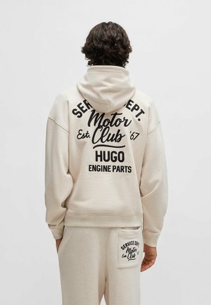 Beige hoodie met een grote zwarte print op de achterkant, met de tekst "Motor Club Est. '67 HUGO ENGINE PARTS." Zacht stof en ontspannen pasvorm.