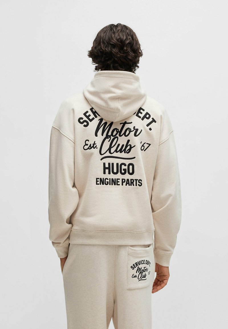 Felpa beige con una grande stampa nera sul retro, che presenta "Motor Club Est. '67 HUGO ENGINE PARTS." Tessuto morbido e vestibilità comoda.