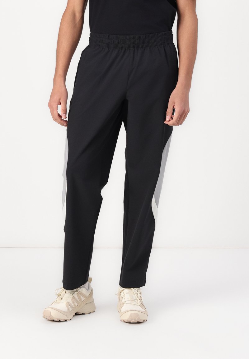 Sorte træningsbukser med elastisk talje, der har grå sidelogoer og en tapered design. Materialet virker let og glat.