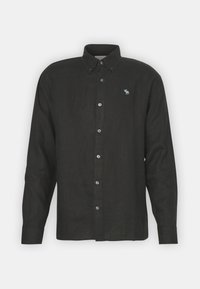 Camisa de lino negra con cuello abotonado, mangas largas y un pequeño animal azul bordado en el pecho. Presenta botones plateados.