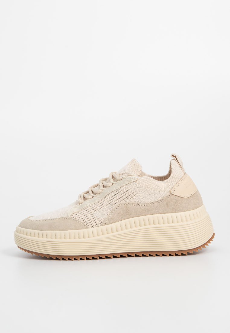 Beige Trainingsschuh mit einem Mix aus strukturiertem Stoff und glattem Wildleder, dicker Gummisohle und Schnürung vorne.
