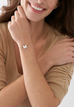 Goldenes Armband mit einem weißen Schmetterlingsanhänger. Das Armband verfügt über eine zarte Kette und ein einfaches, elegantes Design.