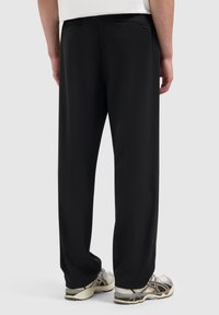 Zwarte broek met een losse pasvorm, zijzakken en subtiele stikdetails. Gekocht in combinatie met lichtgekleurde sneakers. Gladde textuur.