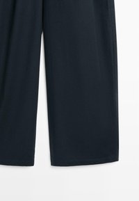 Tmavě námořnické široké kalhoty s nohavicemi zkrácenými nad kotník a rovnými lemy na bílém pozadí.