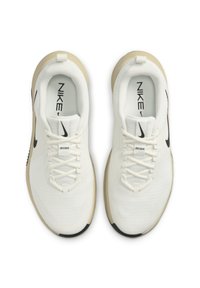 White athletic shoes with a textured mesh upper, black Nike logo, flat laces, and a beige rubber sole. Features a pull tab at the heel.