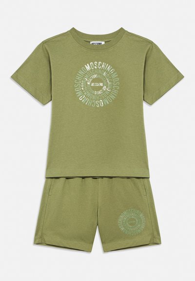 Ensemble chemise manches courtes et shorts vert olive avec logo circulaire "Moschino" imprimé sur la poitrine et la cuisse gauche.
