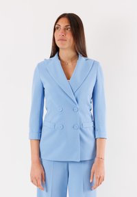 Blazer doppiopetto su misura in tessuto blu chiaro, con rever a propulsione, maniche a tre quarti e due tasche frontali con dettagli a bottoni.