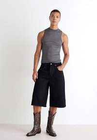 Gray sleeveless top, black wide-leg denim shorts, brown patterned cowboy boots. Plain background, model poses with one hand in pocket.