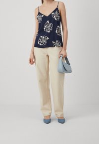 Námořnický květinový top na tenké ramínka, spárovaný se světle béžovými kalhotami s širokými nohavicemi a světle modrými lodičkami s špičatou špičkou. Drží světle modrou kabelku.