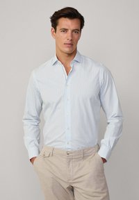 Chemise à manches longues bleu clair et blanche à rayures, avec une texture douce, présentant un col classique et des poignets boutonnés.