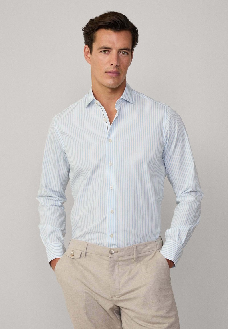 Chemise à manches longues bleu clair et blanche à rayures, avec une texture douce, présentant un col classique et des poignets boutonnés.