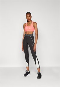 Top sportivo di un vivace rosa con logo "PUMA" bianco, abbinato a leggings neri a vita alta con pannelli bianchi e scarpe sportive.