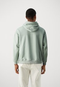Sudadera con capucha de algodón verde claro de corte holgado, con puños y dobladillo acanalados, y detalles de costura en la parte posterior.