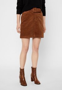 Bruine corduroy mini-jurk met een ceintuurtje in de taille, voorzien van een gestructureerd oppervlak. Gecombineerd met bruine haklaarzen.