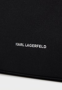 Bolso de tela negro con una textura suave, forma rectangular y un logotipo bordado destacado en blanco: "KARL LAGERFELD."