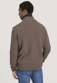 Brauner Strickpullover mit hohem Kragen, gerippten Bündchen und Saum; über einem dunklen Hemd getragen. Lässiger Schnitt, strukturmaterial und nahtlose Schultern.