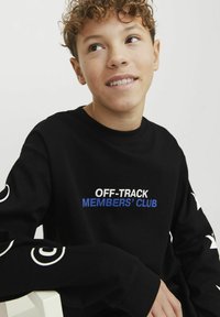 Sudadera negra de manga larga con "OFF-TRACK MEMBERS' CLUB" en texto blanco y azul, con acentos gráficos blancos en las mangas. Tejido suave.