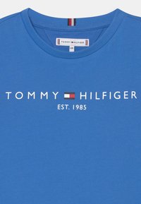 Modré bavlněné tričko s kulatým výstřihem, se středovým bílým textem a logem "TOMMY HILFIGER", s datem založení vytištěným níže.