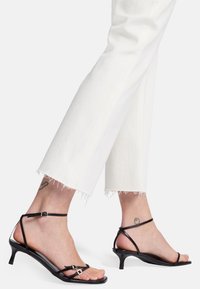 Zwarte sandalen met bandjes en een lage kittenheel, met een slank ontwerp en kleine zilveren gespen, gedragen met witte cropped broeken.