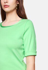 Green short-sleeve top made from soft material, featuring a rounded neckline and rolled cuffs, with visible stitching accents.
