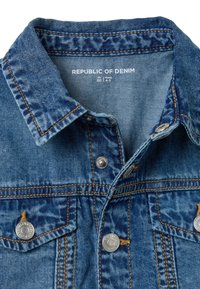 Veste en denim de couleur bleue délavée, devant à boutons, deux poches poitrine, quincaillerie en argent et détails de surpiqûres contrastés. Texte : "Représentant"
