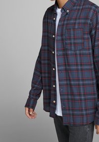 Námořnicky modrá a červená kostkovaná flanelová košile s dlouhými rukávy, límečkem na knoflíky a náprsní kapsou. Měkká textura, dřevěné knoflíky, volný střih.