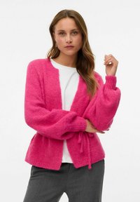 Cardigan en tricot rose avec de larges manches côtelées et une fermeture à nouer. La texture semble douce, avec un devant ouvert et une coupe ample.