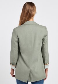 Blazer de lino verde con un corte ajustado, una abertura en la parte trasera y acentos a rayas en los puños. Presenta mangas largas y un cuello clásico.